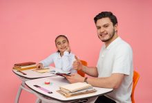 Estudante conversa com um adulto diante de um computador em uma sala de aula.