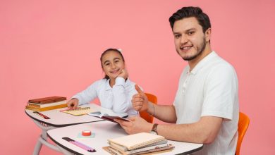 Estudante conversa com um adulto diante de um computador em uma sala de aula.