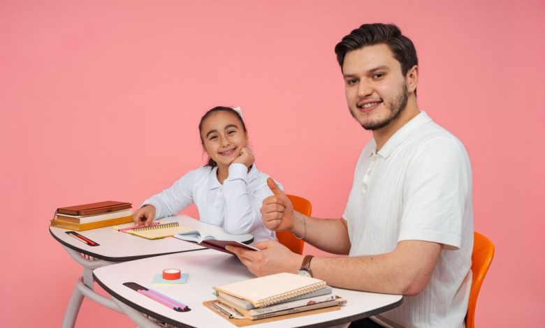 Estudante conversa com um adulto diante de um computador em uma sala de aula.