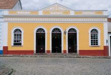 Fachada amarela de um teatro colonial, com janelas em arco e detalhes ornamentais.