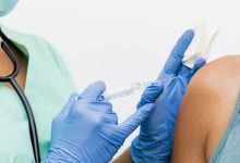 Profissional de saúde usando luvas aplica uma vacina no braço de um paciente.
