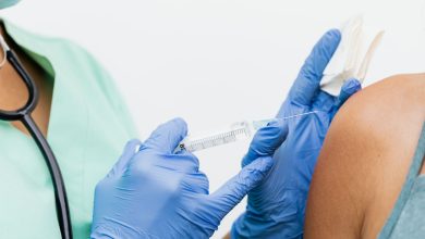 Profissional de saúde usando luvas aplica uma vacina no braço de um paciente.