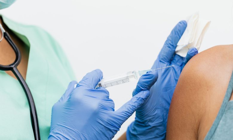 Profissional de saúde usando luvas aplica uma vacina no braço de um paciente.