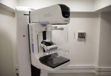 Profissional de saúde ao lado de um aparelho de mamografia em ambiente hospitalar.